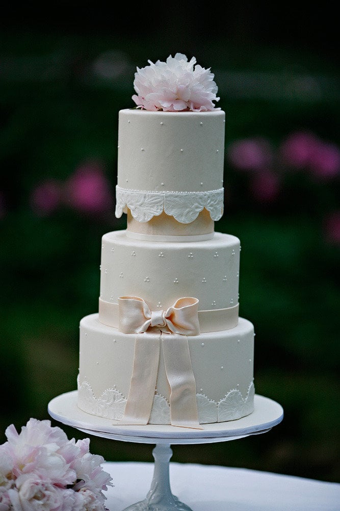 It's got pearls, it's got a bow, it's got a lace-like pattern, it's got flowers — yet this cake still manages to be sweet and romantic in the simplest way. 
Photo by Marie Labbancz Photography via Style Me Pretty