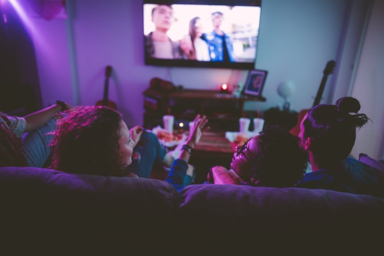 Young multi-ethnic hipster friends relaxing on living room sofa and watching film on TV