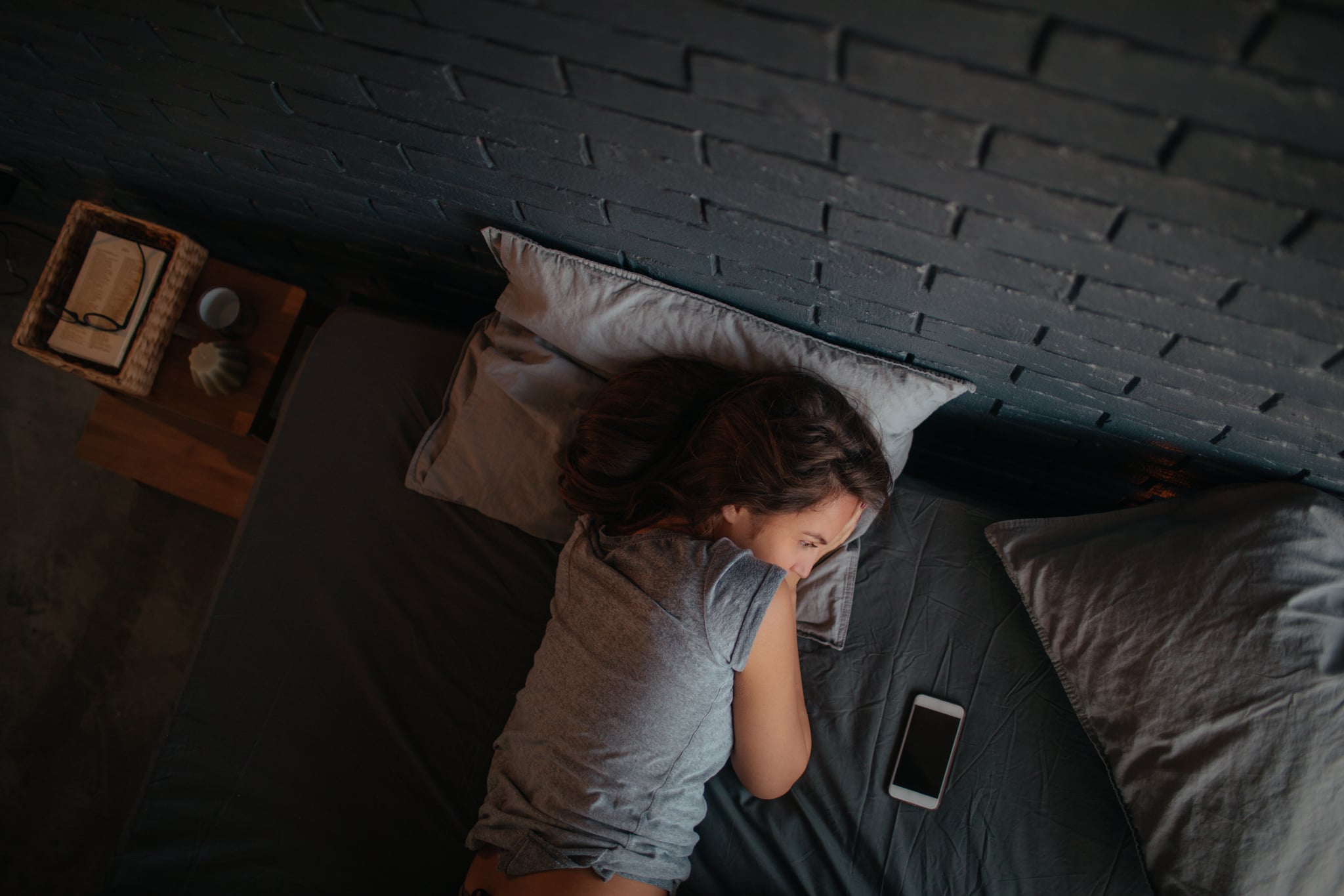 Photo of a young woman lying down in her bed and waiting for the call on her mobile phone