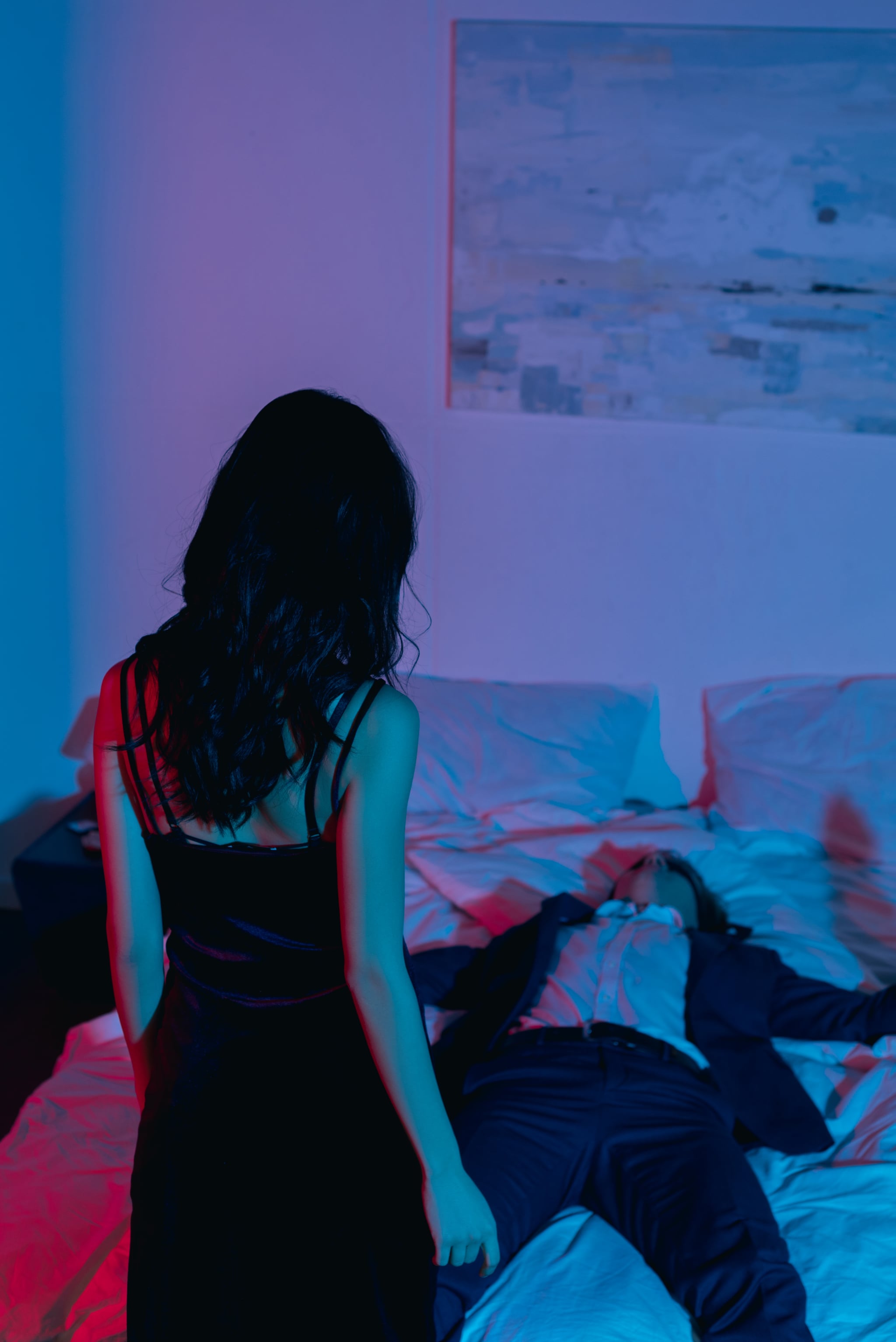 back view of woman in evening dress looking at boyfriend in bed blindfolded