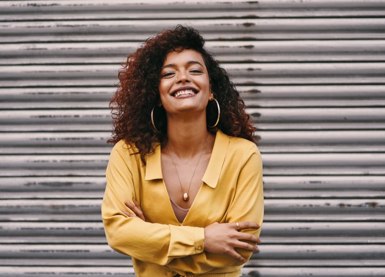Cropped portrait of an attractive young woman smiling while standing with her arms folded against an urban background
