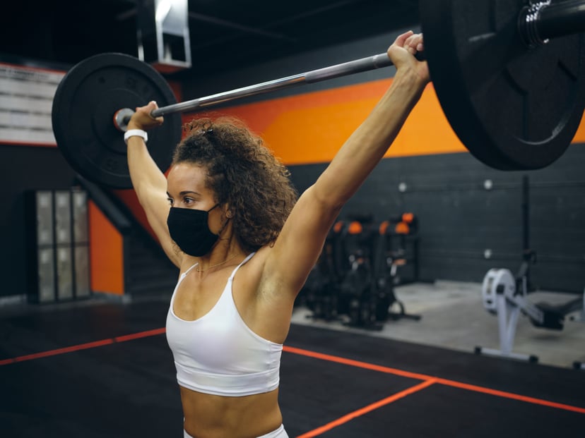 Women working out in a gym, doing weight training with a barbell.