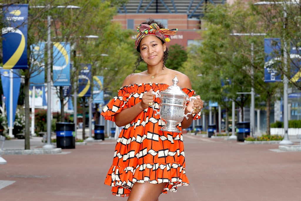 Naomi Osaka is a two-time US Open women's singles champion, and her celebratory postgame outfit would put anyone in a winning mood. On the day following her final match, the 22-year-old athlete posed with the iconic silver trophy in an orange patterned dress and a colorful head wrap. "You already know I had to bring out the headwrap for this one," she tweeted on Sunday, alongside a picture from the photo shoot.
Naomi's look was praised on social media by commenters who appreciated the deliberate nod to her Japanese-Haitian heritage. Earlier in the day, she tweeted, "I would like to thank my ancestors because everytime I remember their blood runs through my veins I am reminded that I cannot lose." What a beautiful message! Naomi consistently uses her platform to start conversations and create a safer space for her community, especially Black victims of police brutality and other violence. As she wrote, "before I am a athlete, I am a black woman." 
See more of her US Open outfit ahead.