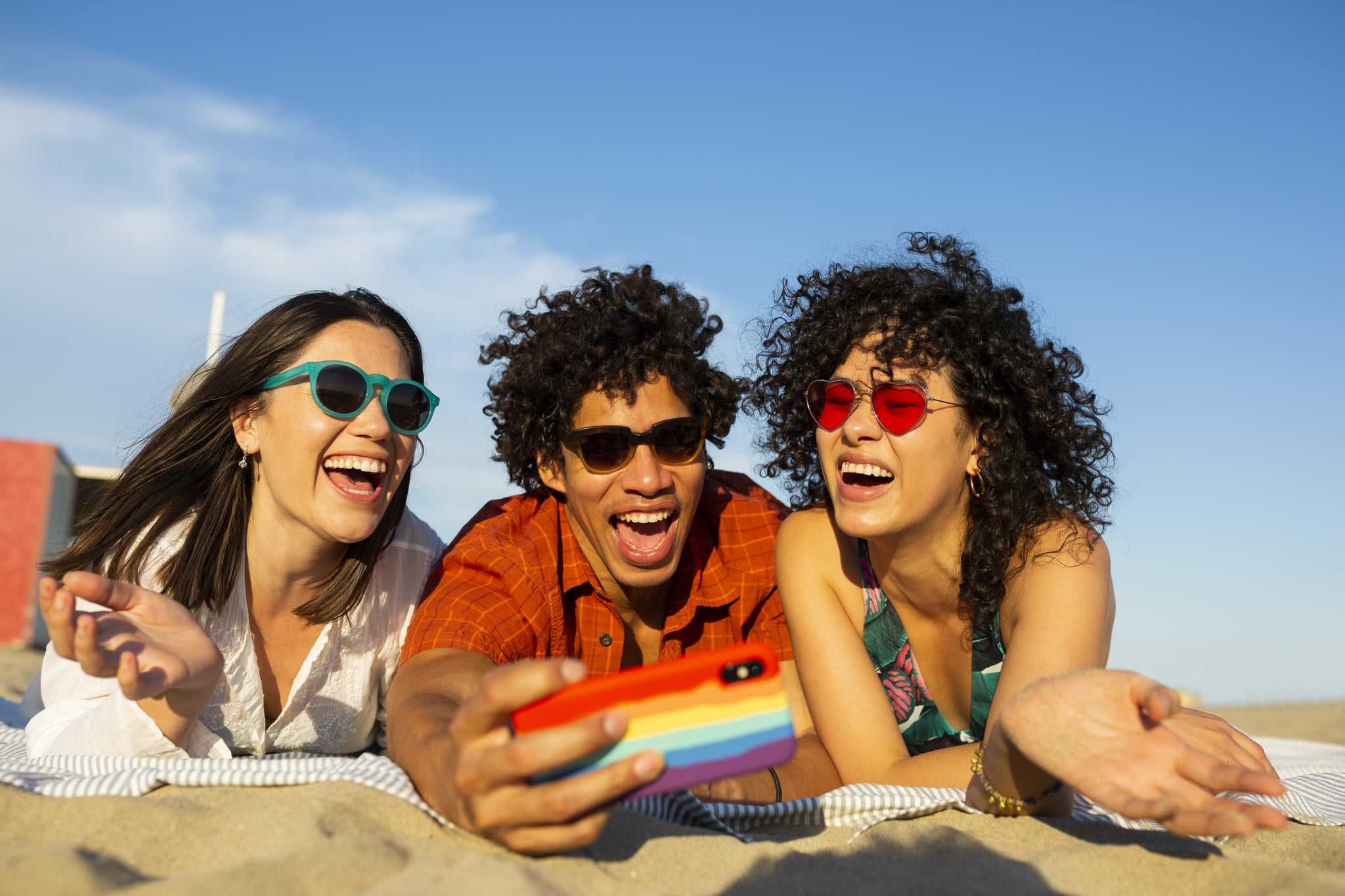 Group of multi ethnic friends, two women and a man, taking a selfie with an smartphone and hanging out at the beach