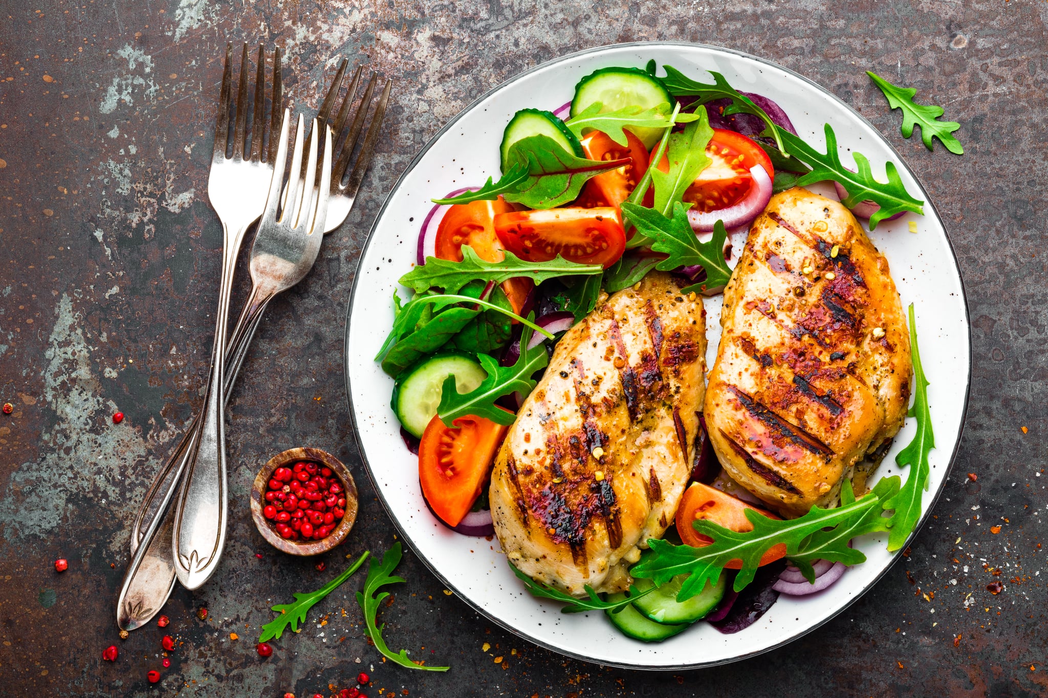 Grilled chicken breast. Fried chicken fillet and fresh vegetable salad of tomatoes, cucumbers and arugula leaves. Chicken meat with salad. Healthy food. Flat lay. Top view. Dark background