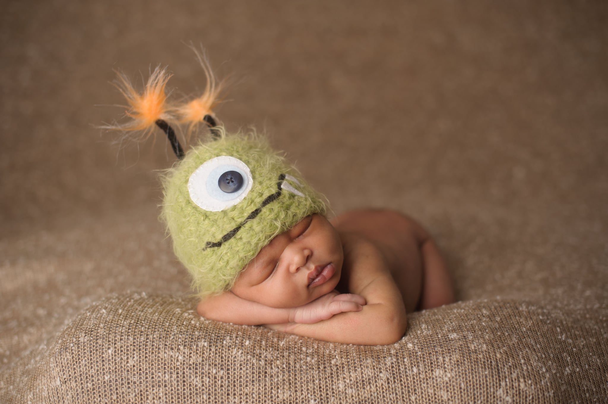 A newborn sleeping in a Halloween-themed monster hat.