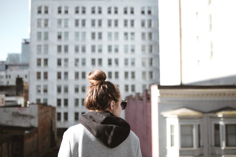 Young adult woman with her hair in a bun wearing sunglasses in front of urban buildings from a rooftop