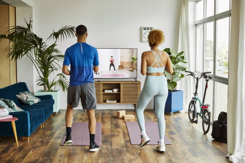 Rear view of young couple doing workout in living room. Man and woman are watching online exercise class on TV. They are in sportswear.