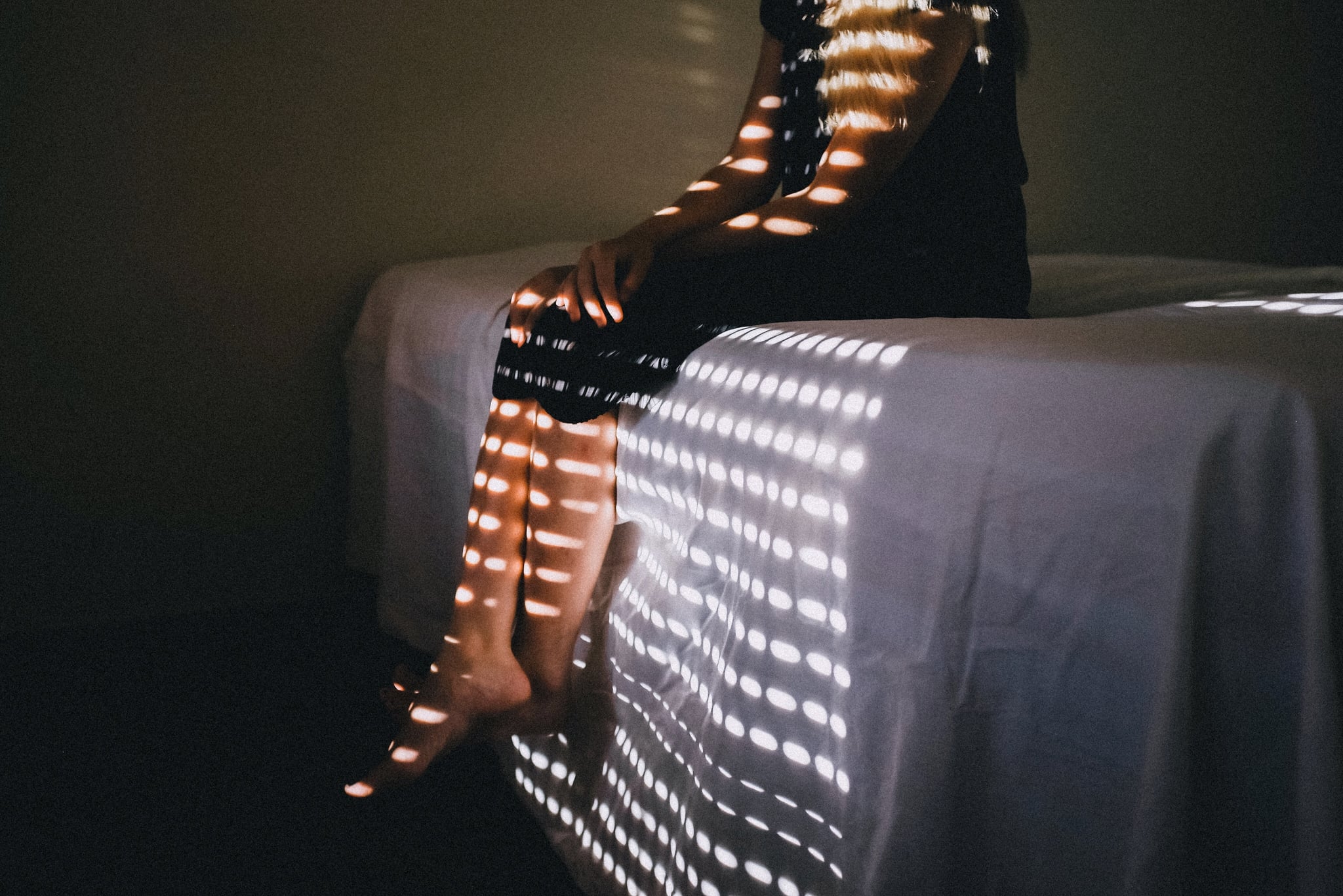 Person sitting on the edge of their bed facing the window