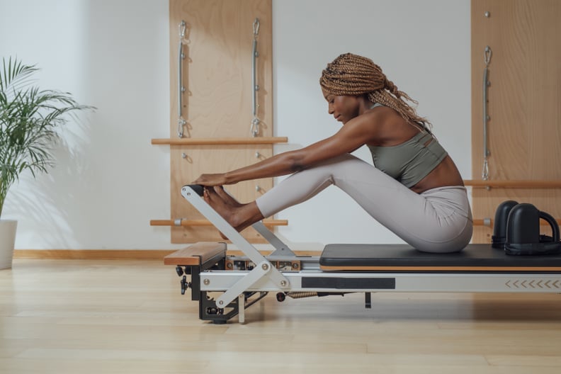 Beautiful African smiling sportswoman doing pilates exercise on reformer as part of the 3-2-1 workout method