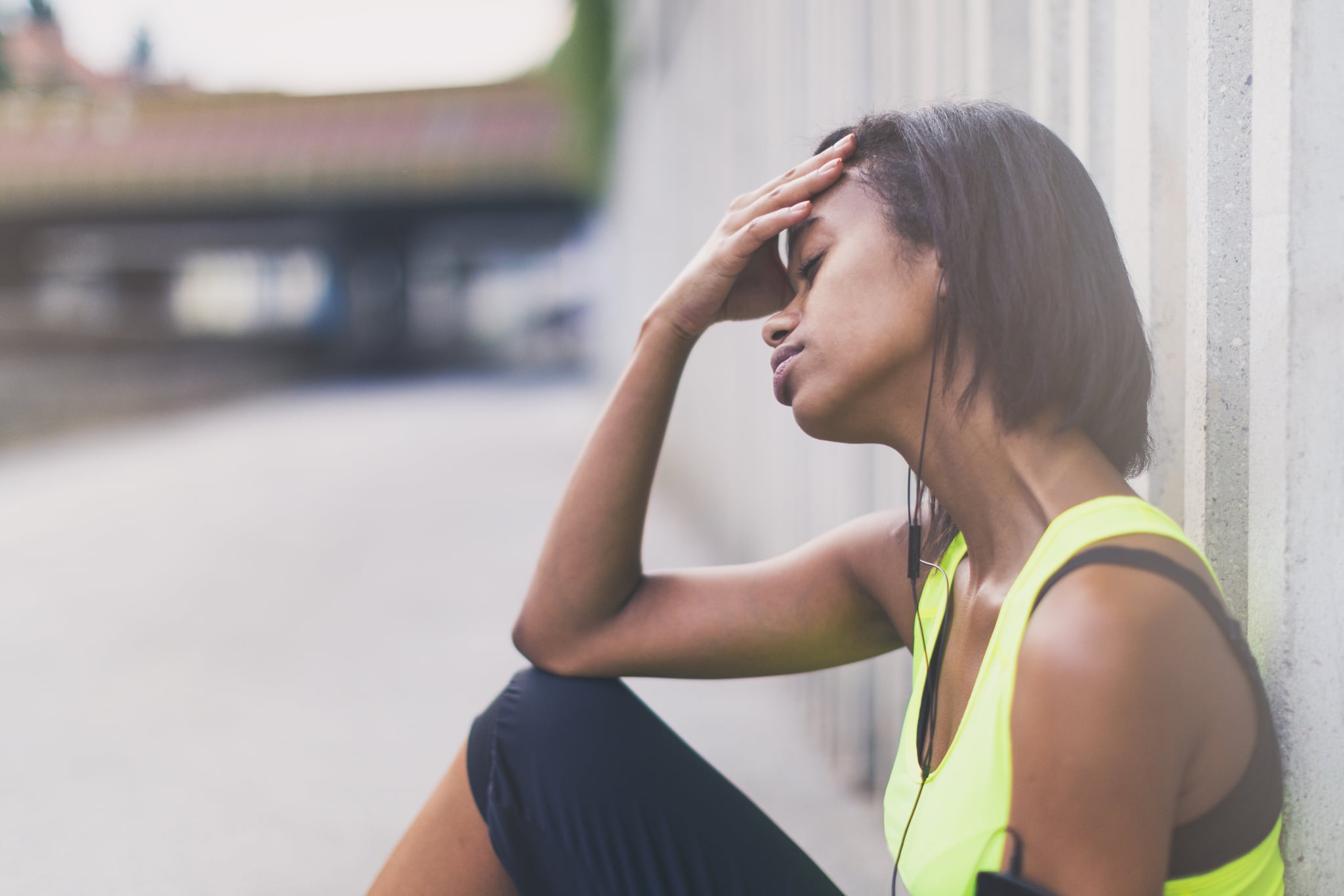 Tired young woman of african descent jogging in the city, leaning on a concrete wall, resting