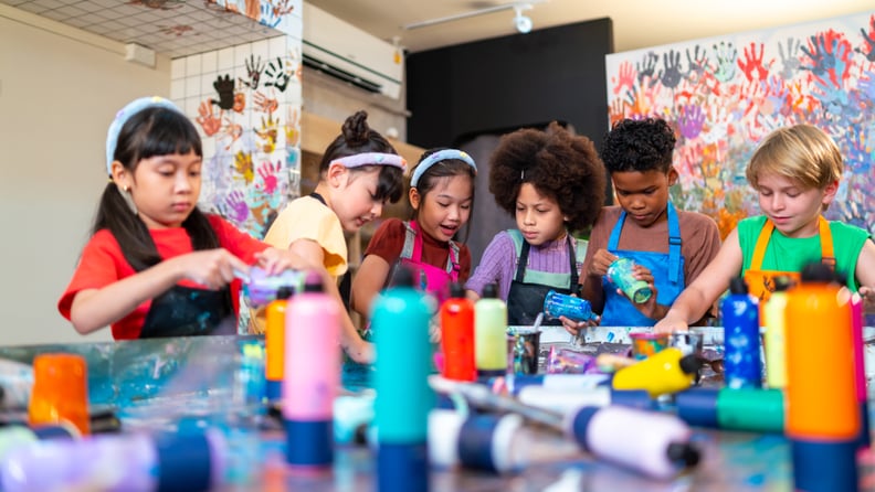 Group of school children learning acrylic pouring art on canvas workshop with teacher at art studio. Happy boys and girls enjoy and fun with colorful abstract modern art painting in classroom.