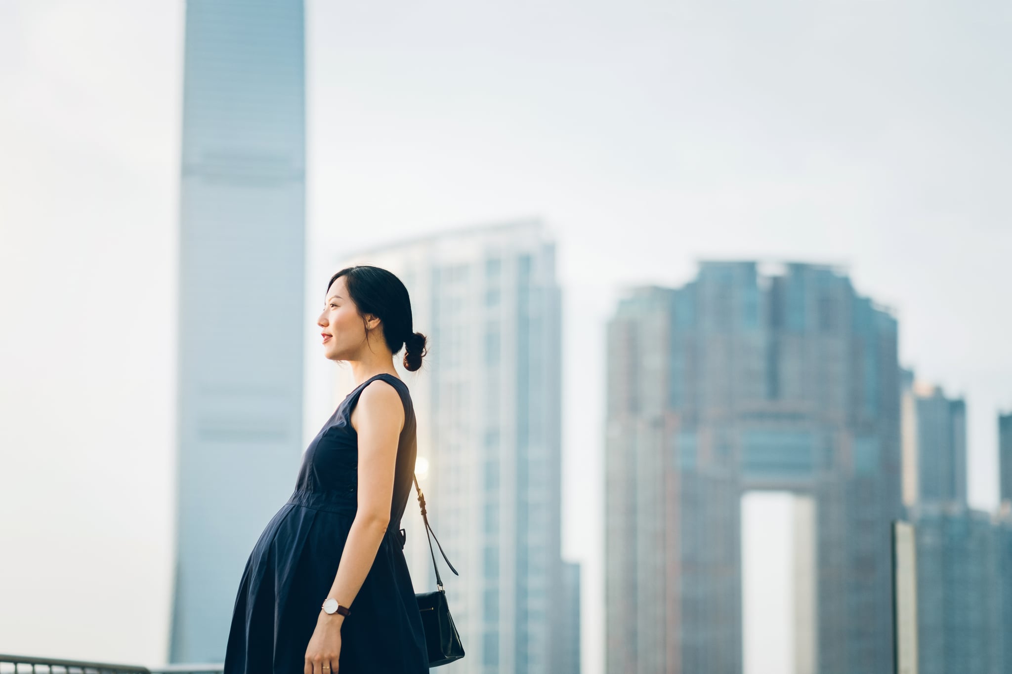 Beautiful pregnant Asian woman standing against modern cityscape enjoying view