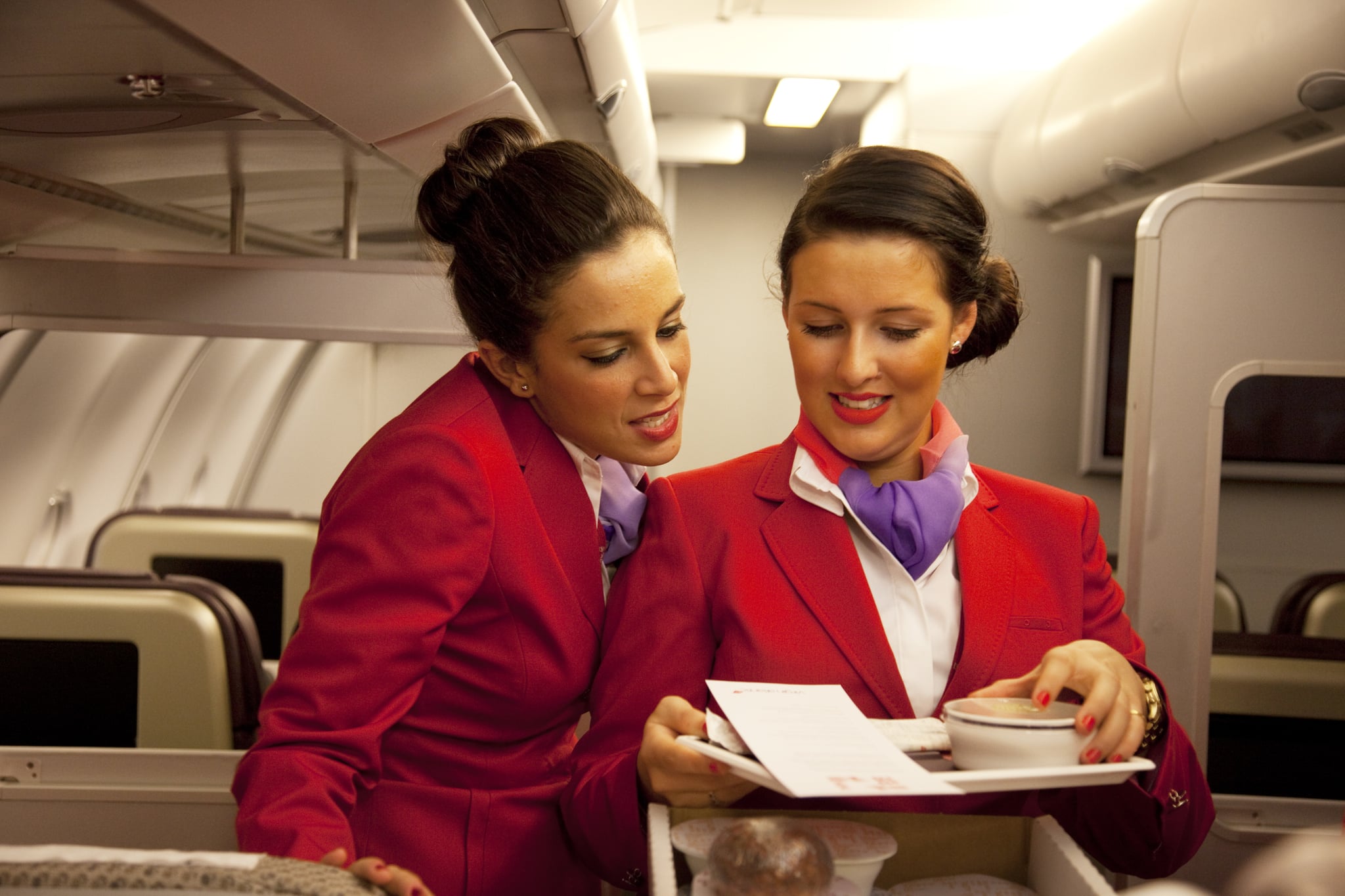 One week away from getting their 'wings' these flight attendants proudly wear their red uniforms as they undergo an in flight training session focussing on how to serve meals and using the service trolley. Virgin Atlantic air stewardess and steward training at The Base training facility in Crawley. Potential hostesses are put through a gruelling 6 week training program, during which they are tested to their limits. With exams every day requiring an 88% score to pass. The Base is a modern environment for a state of the art airline training situated next to Virgin Atlantic's HQ. (Photo by In Pictures Ltd./Corbis via Getty Images)