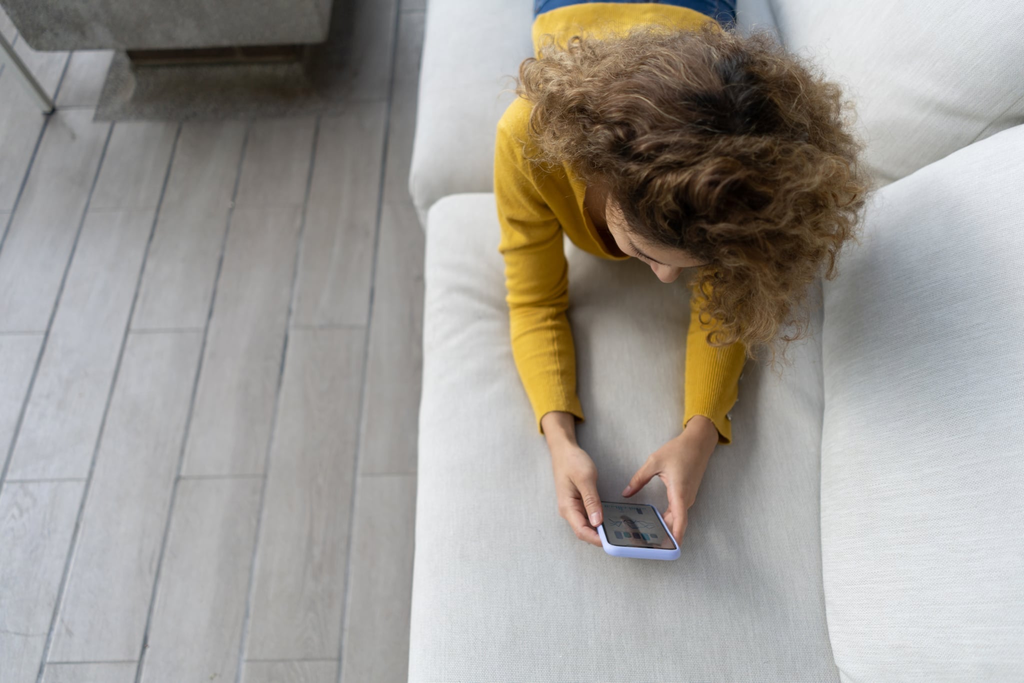 Young woman looking at social media on her cell phone while lying on the couch at the terrace of her house - lifestyle concepts