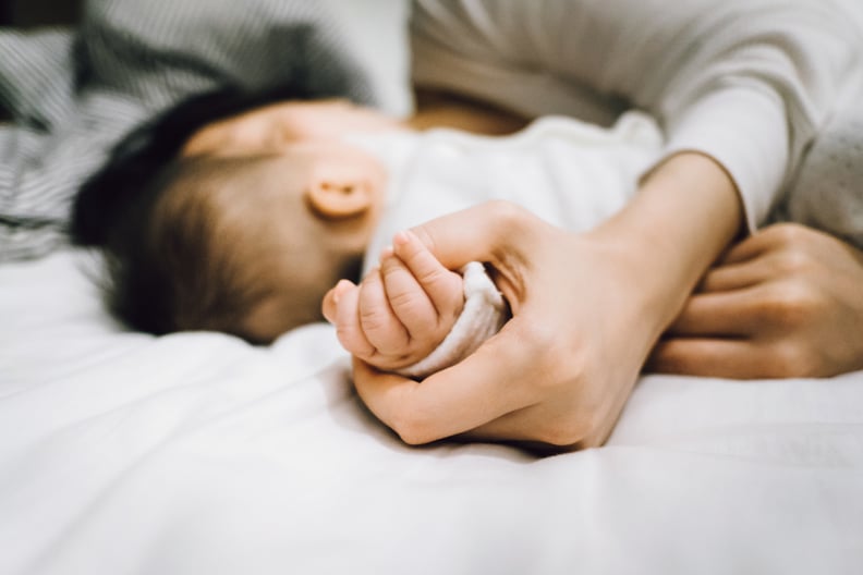 Mother holding hand with baby girl on bed