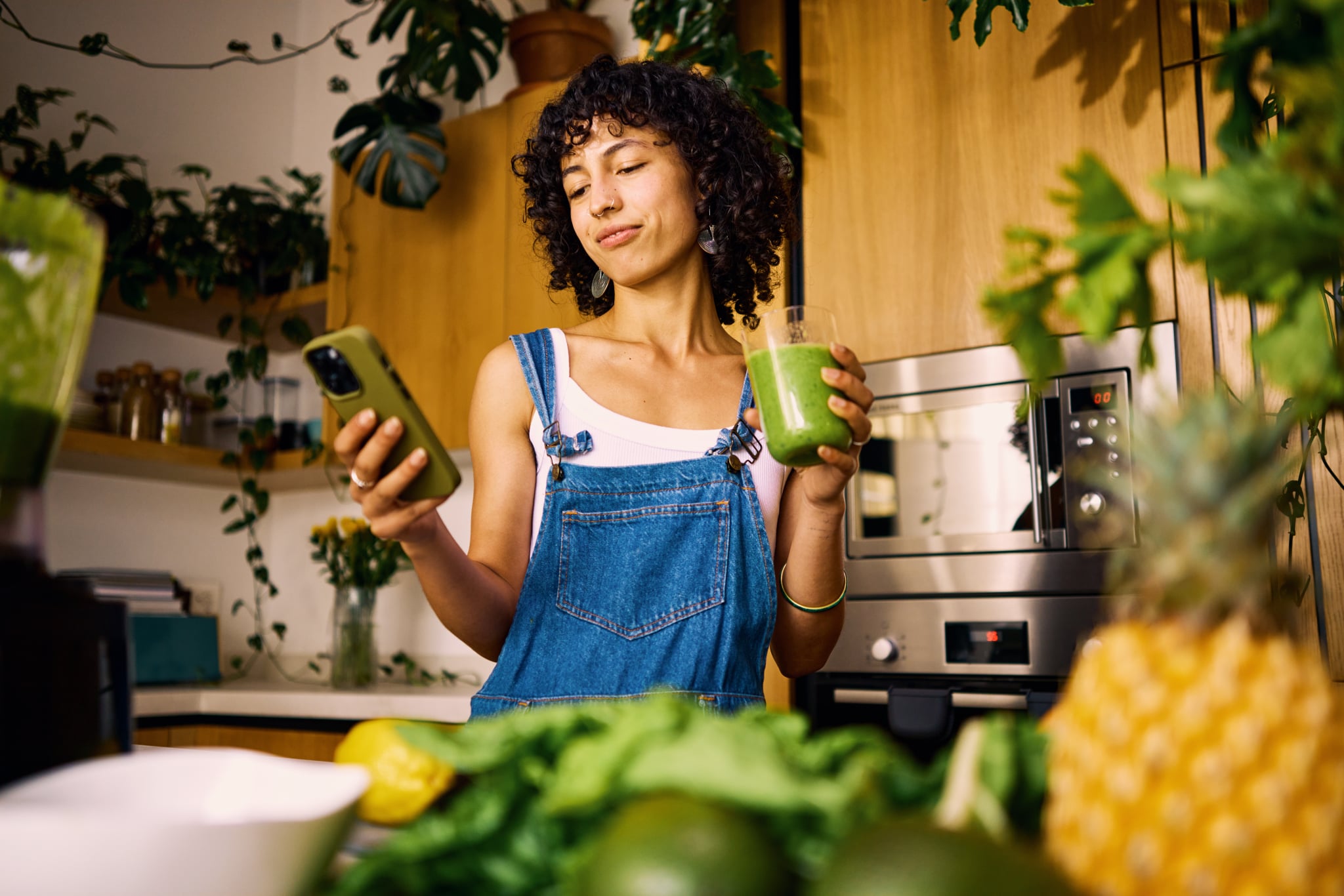Woman drinking green juice in kitchen and looking at her phone for advice.