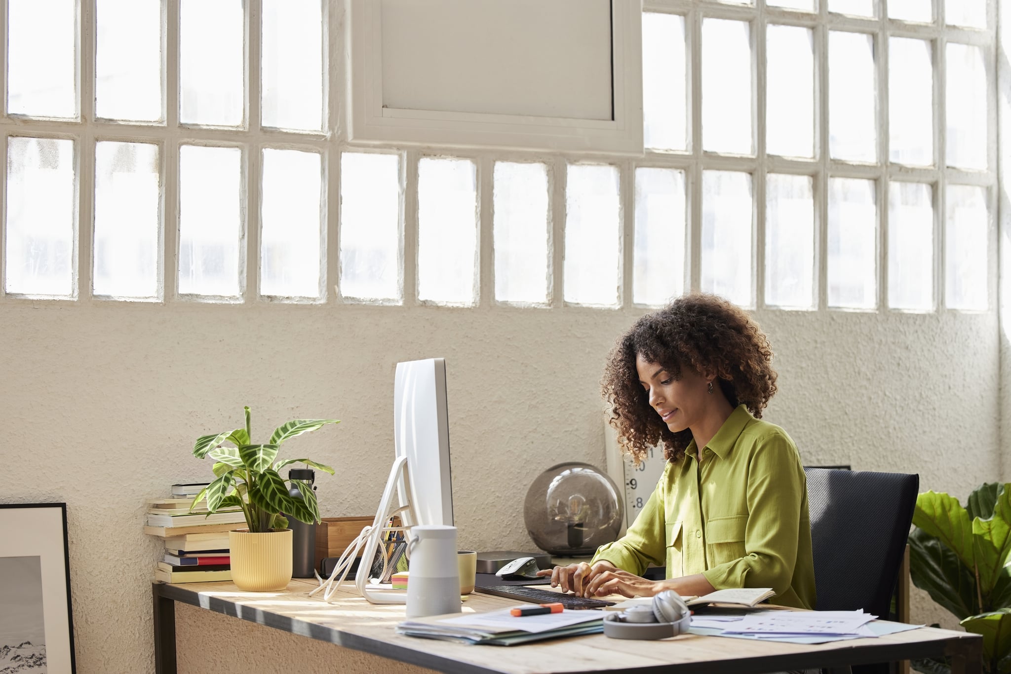 Female professional with curly hair typing while sitting at desk. Entrepreneur is working from home. She is using computer.