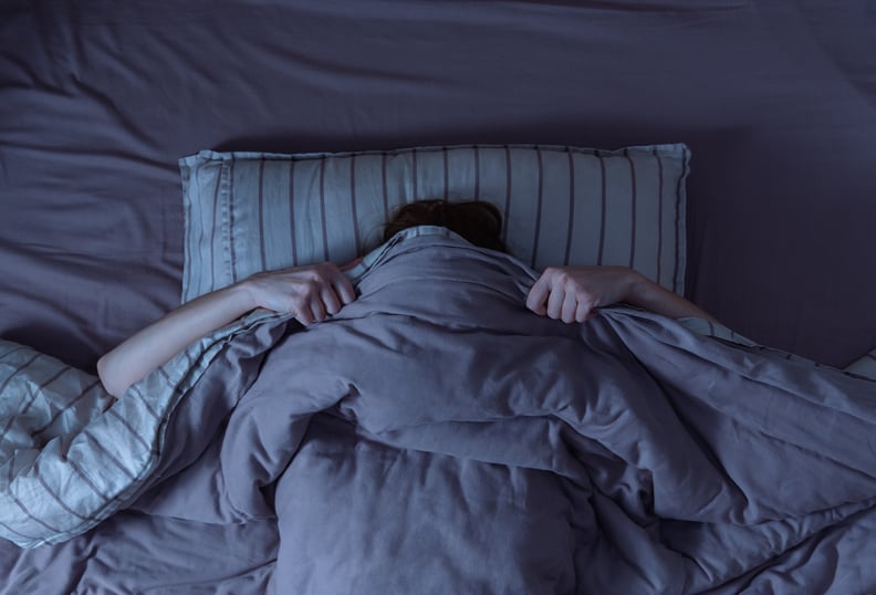 Top view of woman in bed covering her face with blanket, scared by melatonin nightmares.