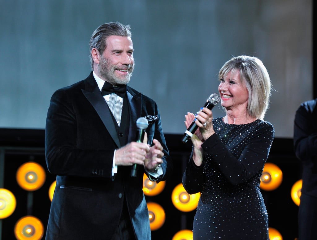 After 40 years, Danny and Sandy still go together like rama lama lama ka dinga da dinga dong. During the G'Day Black Tie Gala on Saturday, John Travolta and Olivia Newton-John had an adorable Grease reunion as they spoke on stage with honoree John Farrar. Aside from sharing a few laughs (and giving us a heavy dose of nostalgia), Olivia even commented on the iconic film's upcoming anniversary, adding that she can finally watch it without cringing. 
"I think I was telling someone before that in the early days when we did the movie, I used to watch it and cringe," she told People. "Like, Why did I do that and I could have done that. But now, with all the time and the people [who] love it, I can relax and enjoy it." Of course, she is incredibly grateful to John as well, whom she met before filming had even started. "I couldn't have done the movie if I hadn't met him, because I really wasn't sure I wanted to do it," she added. "He kind of came to talk me into it." See more pictures from their sweet reunion ahead.