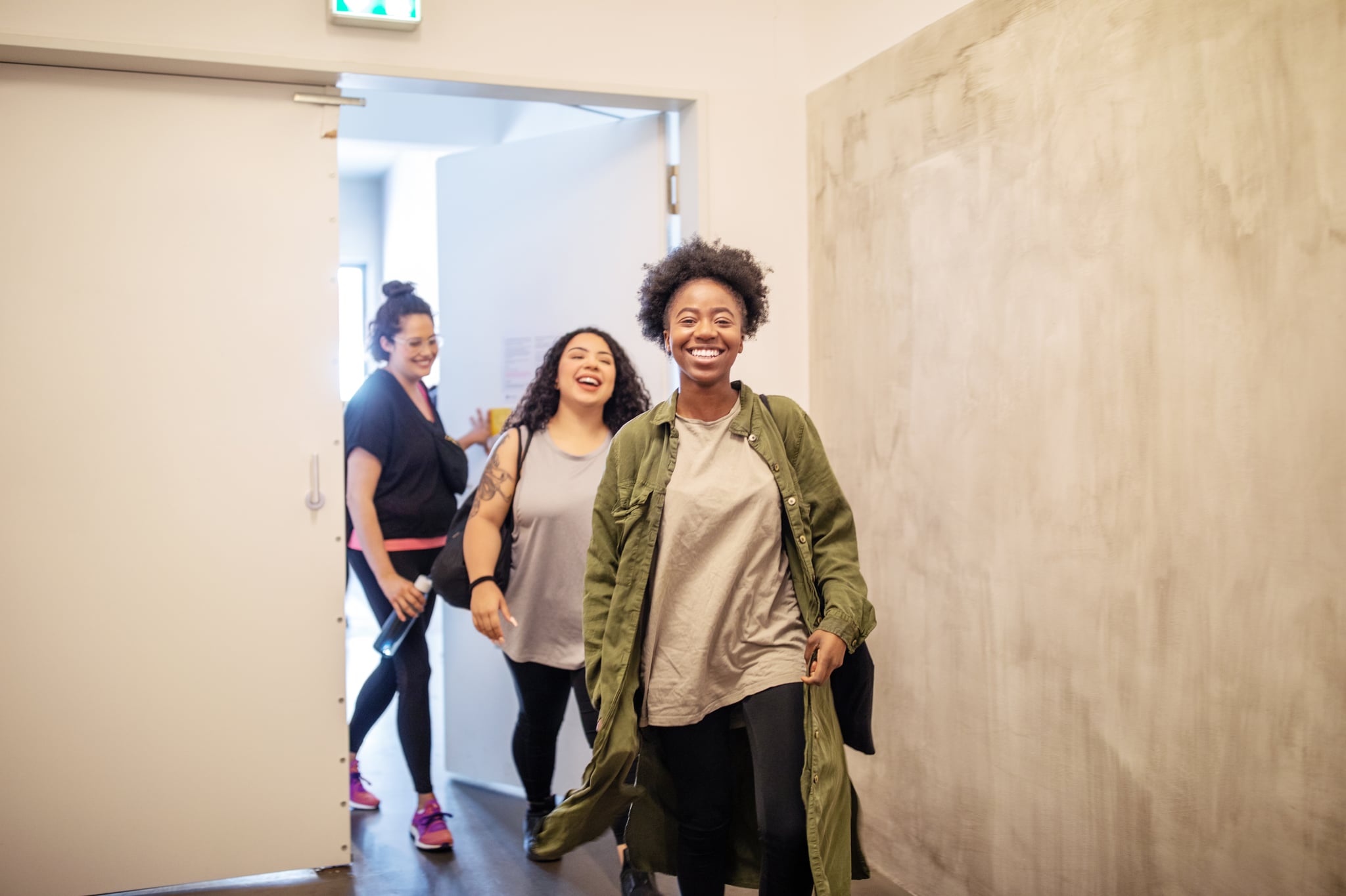 Group of multiracial females entering fitness studio. Smiling women walking through a doorway in dance class.