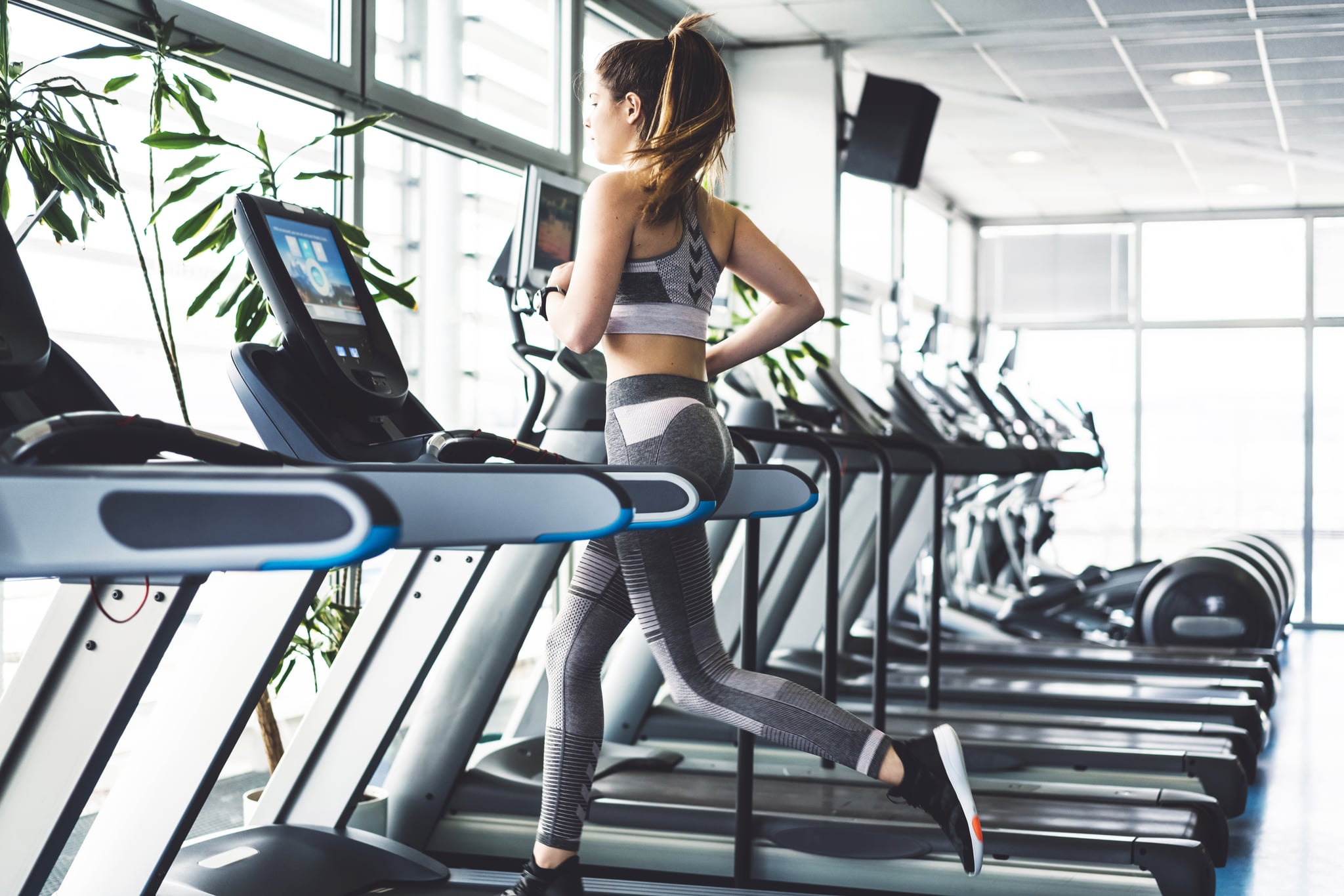 Beautiful young woman training in the gym. Exercise is a part of her daily routine. Before you start with your workout it is important to warm up your body properly, so you don't get injured, do a lot of stretching. Exercise is important for your health and mind. Young brunette girl is working hard in the gym. Her workouts are hard. Skinny young women training to be the best. She is dressed in sports clothing, se is wearing pastel pink colour leggings and top. Her sports shoes are black colour. She has her hair tied up in a ponytail. Trx is a popular gym equipment, lots of different exercises can be made with it.