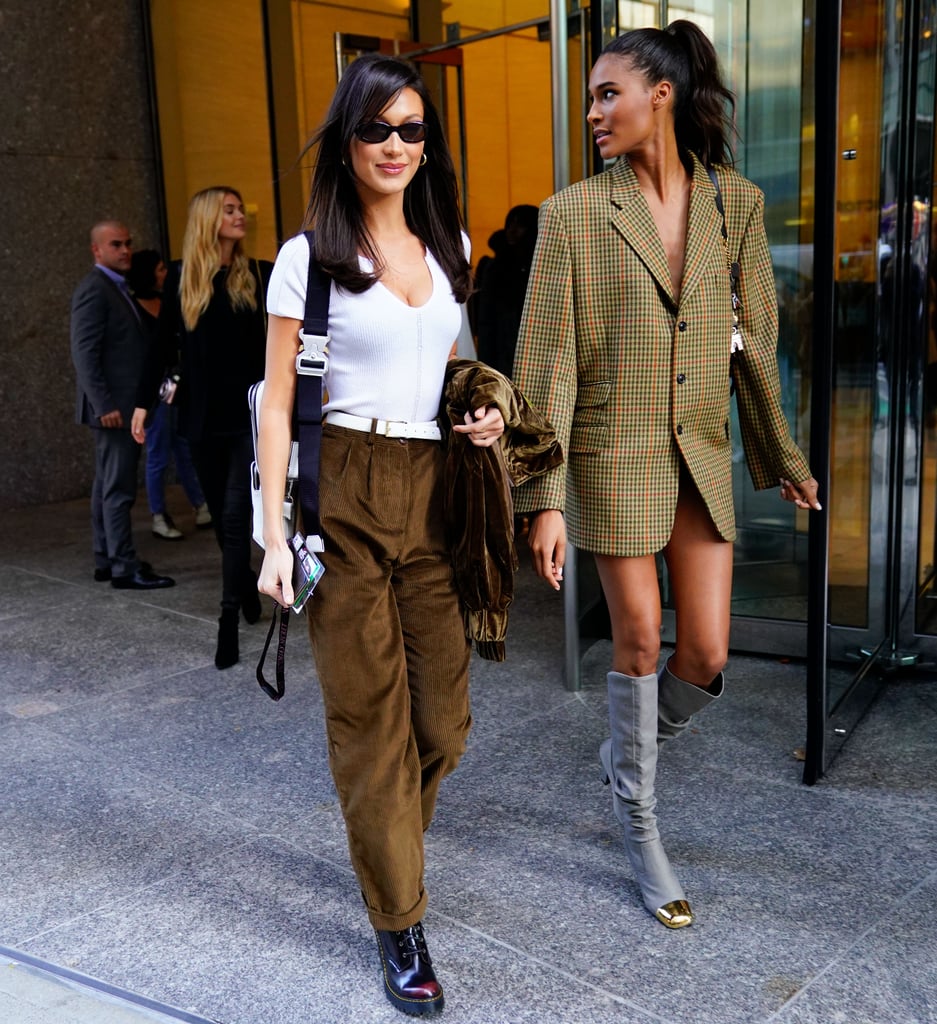 Bella Hadid wearing a white top with brown suede pants and tiny sunglasses. Cindy Bruna opted for a blazer dress with thigh-high boots.