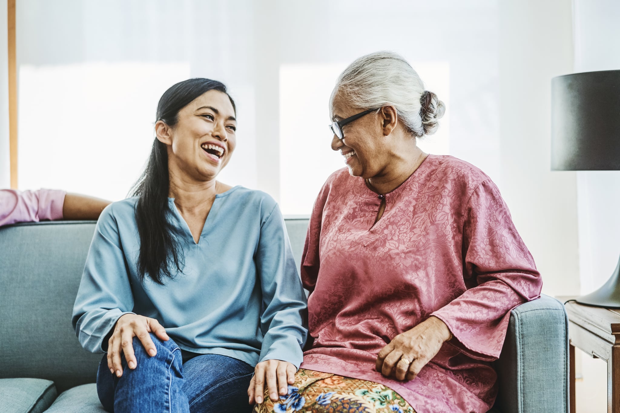 Happy mature woman sitting with mother-in-law on sofa. Females are talking in living room. They are spending leisure time.