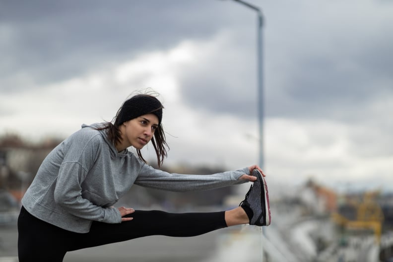 Handsome young Caucasian sportswoman doing warm up exercises outdoors on a cold weather day in the city