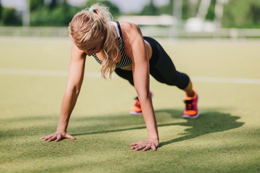 Blond haired woman doing pushup or press-up on a sports field.
