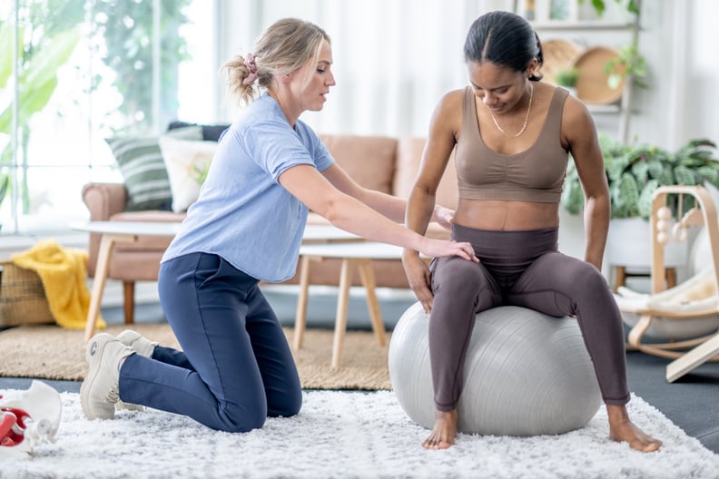 A female physiotherapist works with a pregnant woman during an appointment.  The woman is dressed comfortably and sitting on a yoga ball as they work through various exercises.