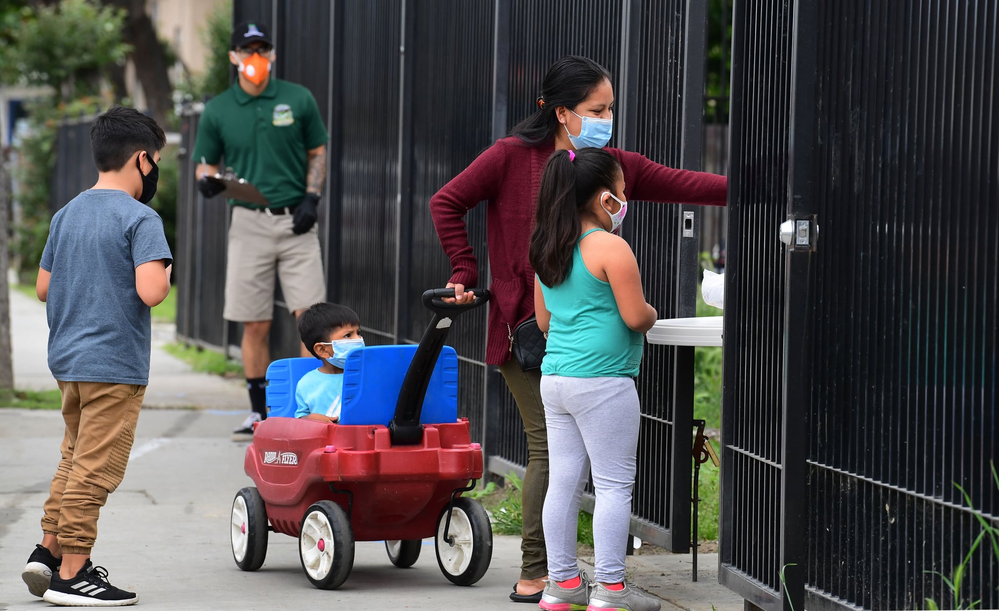 A woman with her children wearing masks, reaches out to pick up a bag of groceries distributed at a food bank opened in response to the coronavirus pandemic on April 20, 2020 in El Monte, California (Photo by Frederic J. BROWN / AFP) (Photo by FREDERIC J. BROWN/AFP via Getty Images)