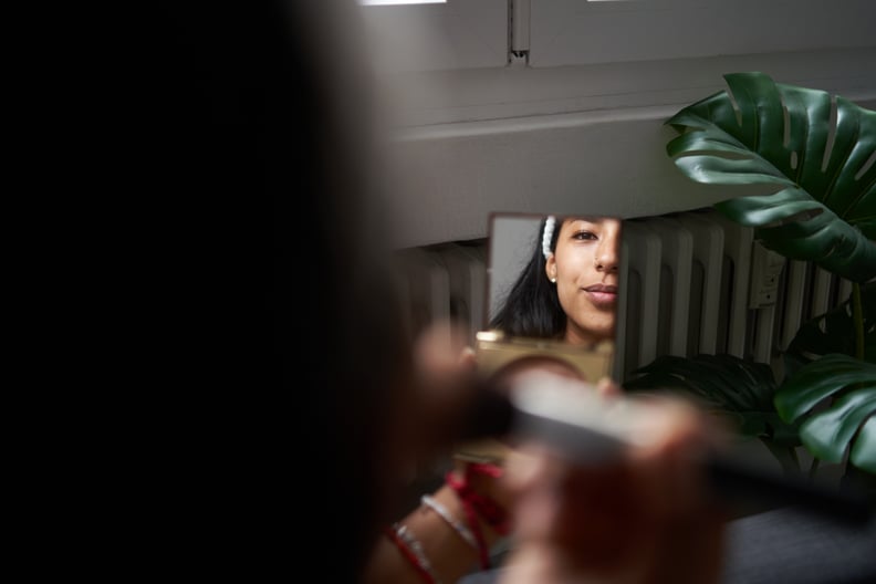 Selective focus on a young woman looking in the mirror while applying makeup at home.