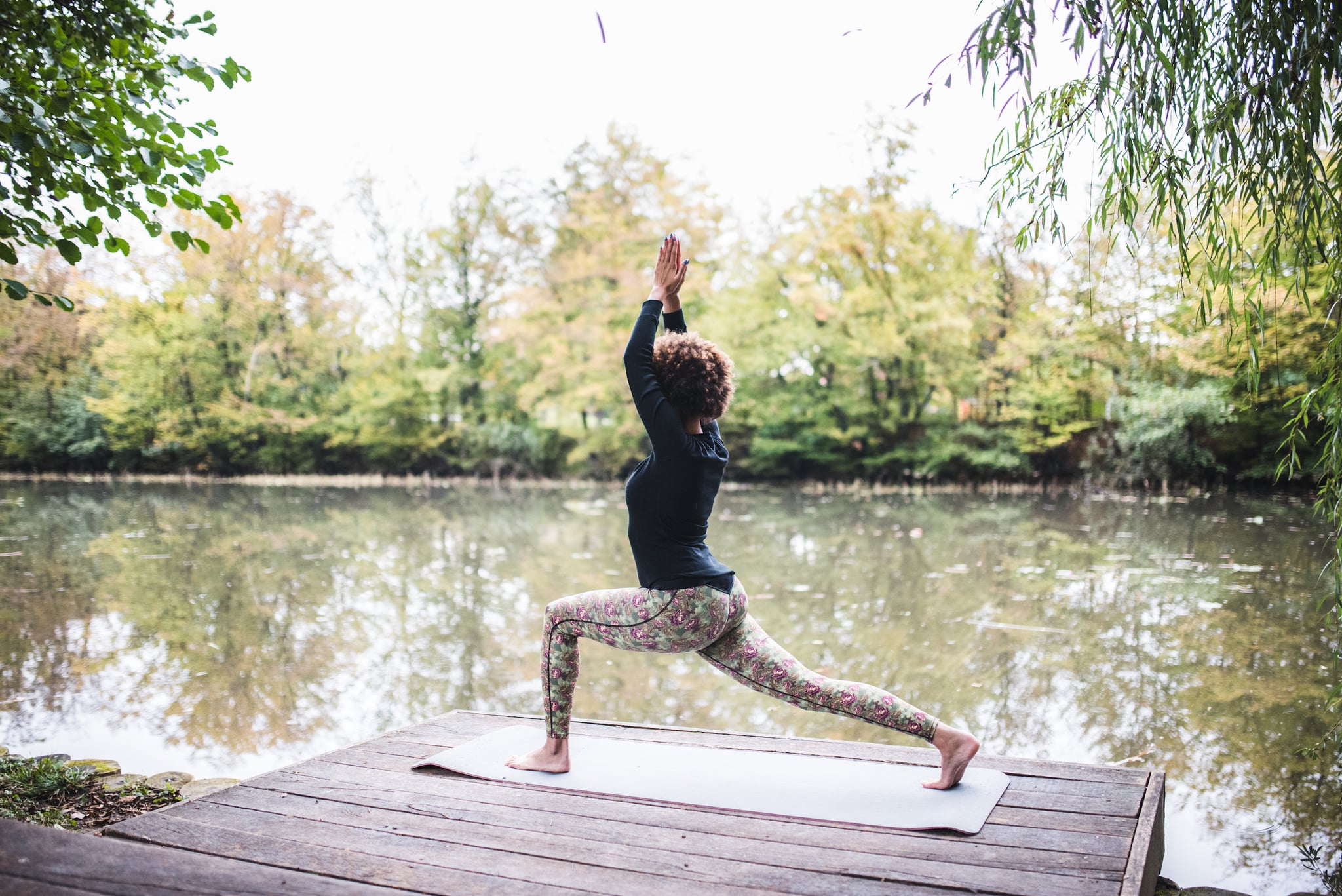 Young woman practising yoga on a mat in front of a lake