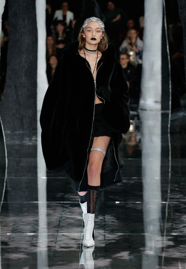 Gigi debuted an edgy look at Rihanna's Fenty x Puma show, wearing layered necklaces, an oversize unzipped coat, sheer socks, a crystal garter, and white lace-up booties.