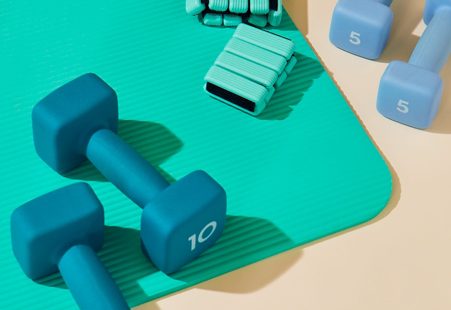 Teal yoga mat and anklet weights beside blue dumbbells.