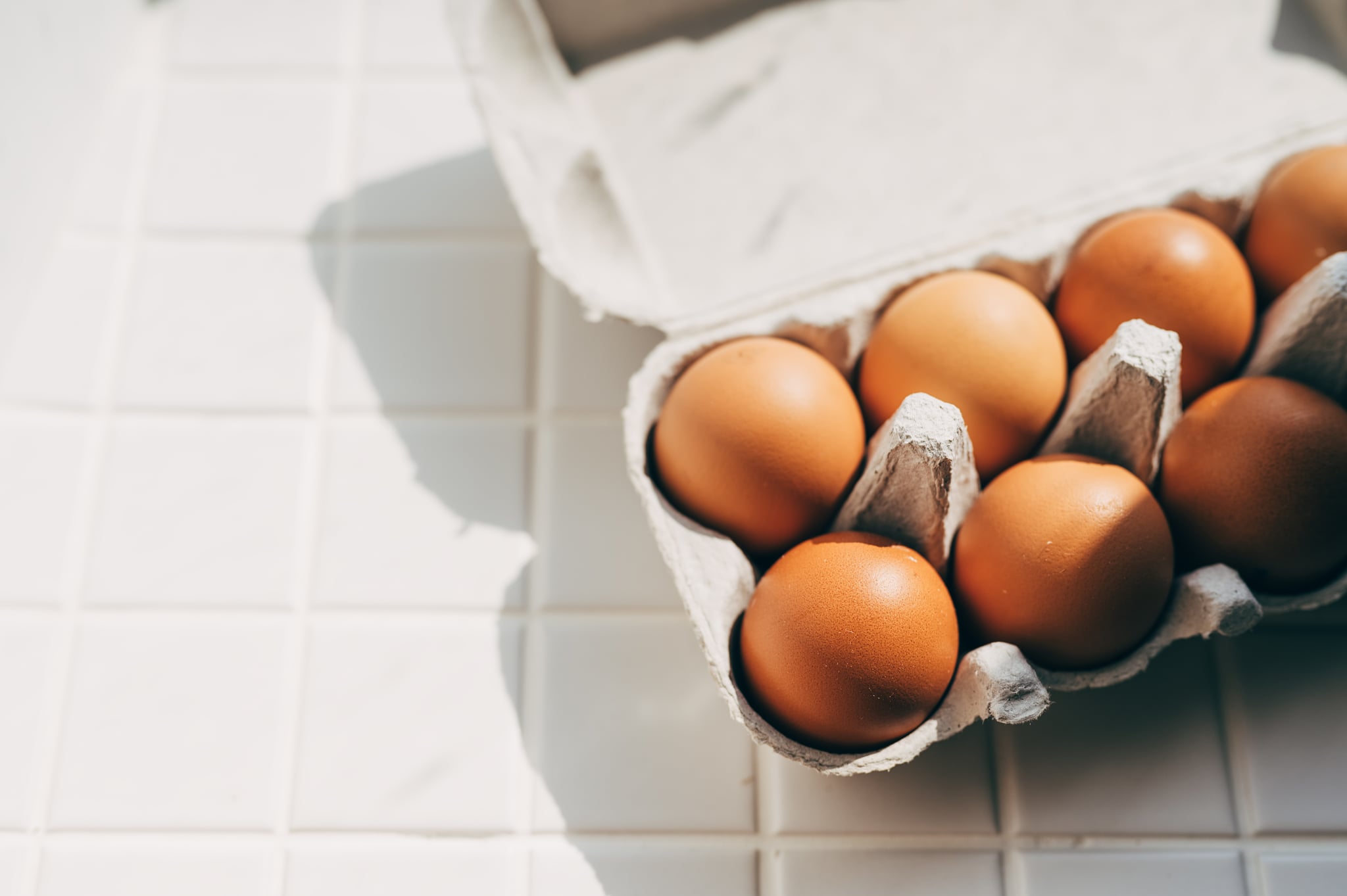 A collection of fresh organic brown chicken eggs neatly arranged in a grey recycled paper pulp carton tray placed on a wooden kitchen table with a blurred modern home interior background.