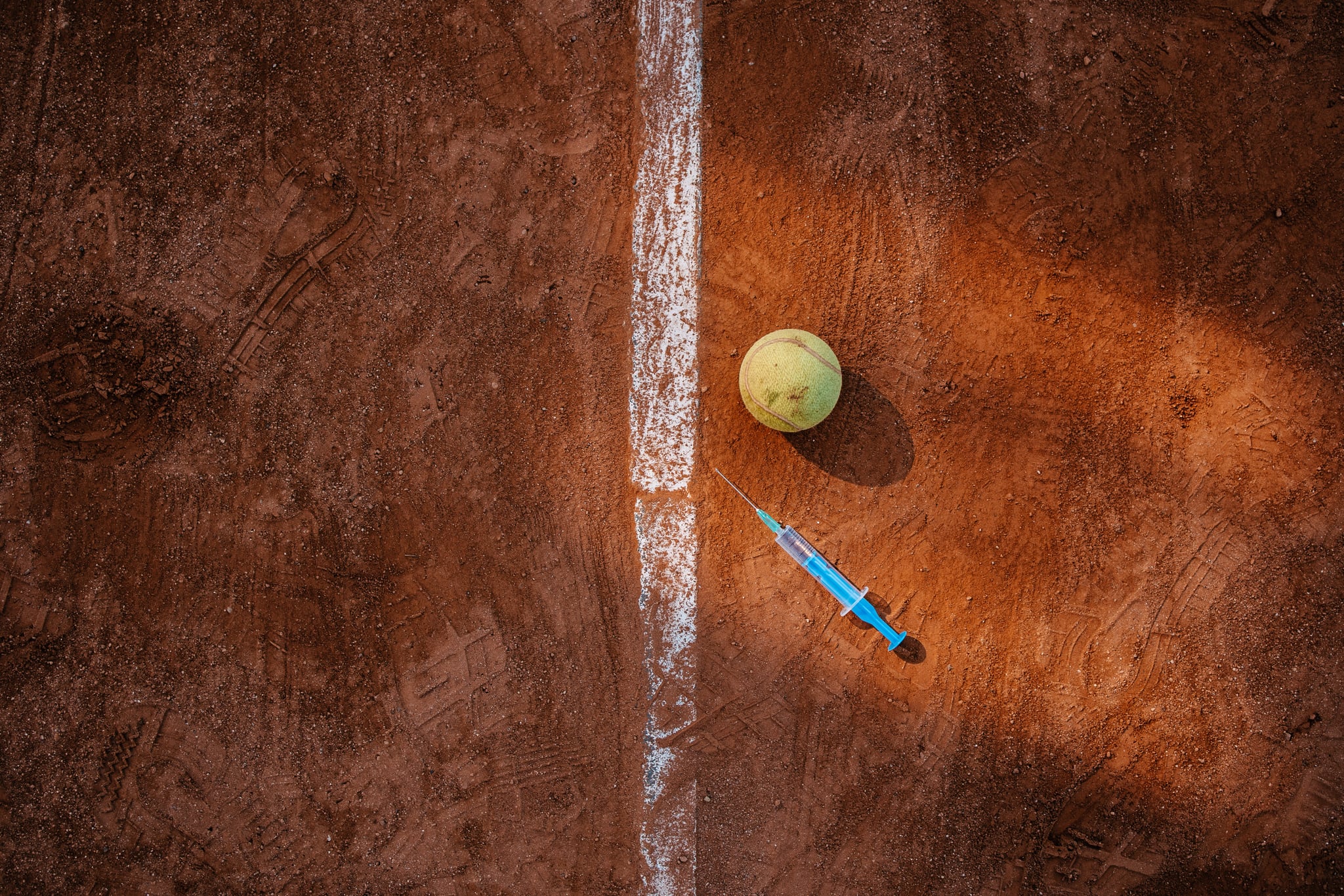 High angle view of a tennis ball and a syringe for vaccine on a clay court.