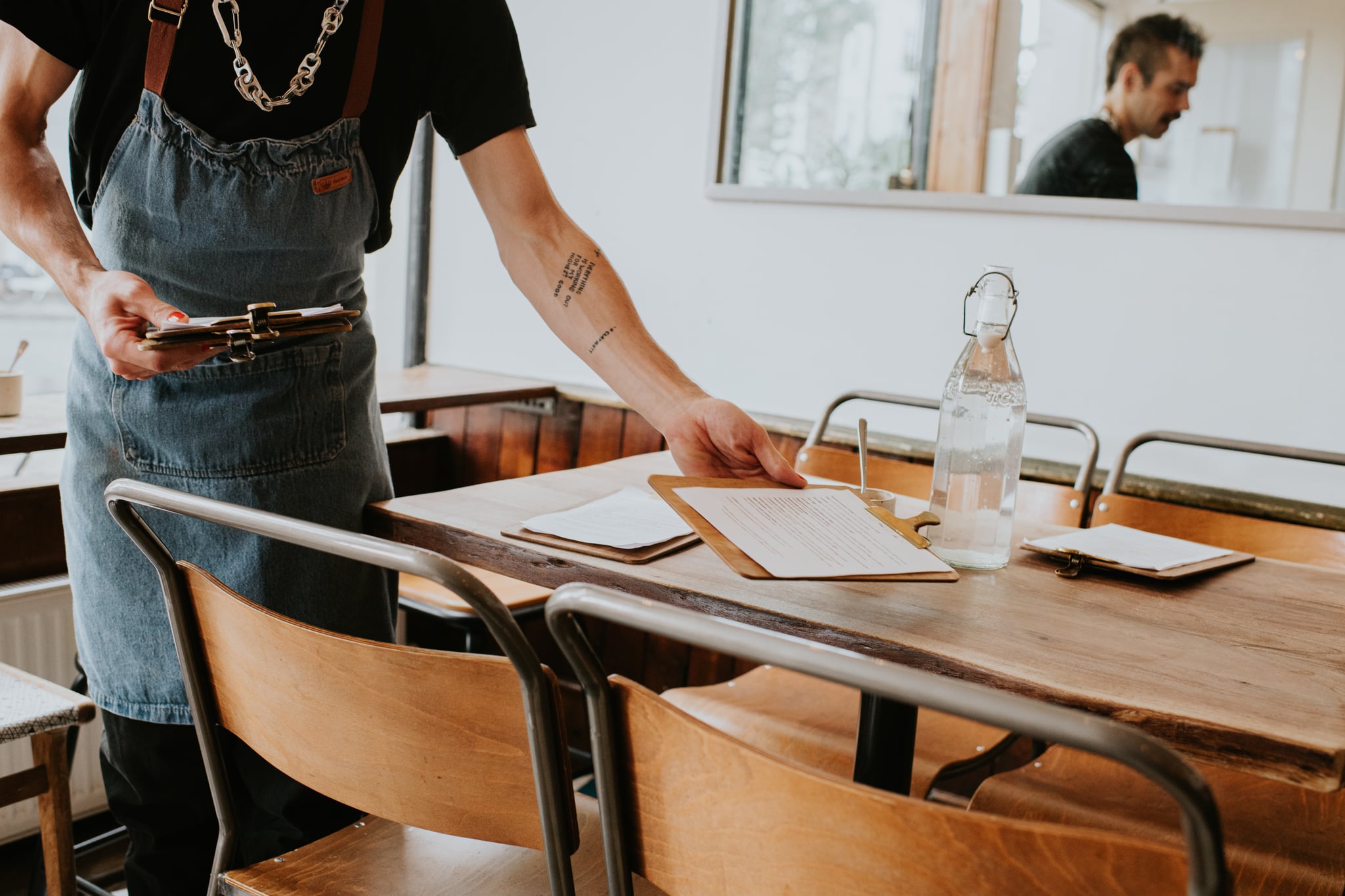 A Man Wearing Apron Places Menus on Table Inside a Restaurant