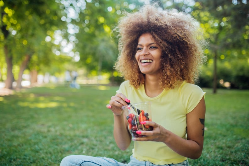 Portrait of a beautiful Afro girl sitting at the park, eating fruits and enjoying.