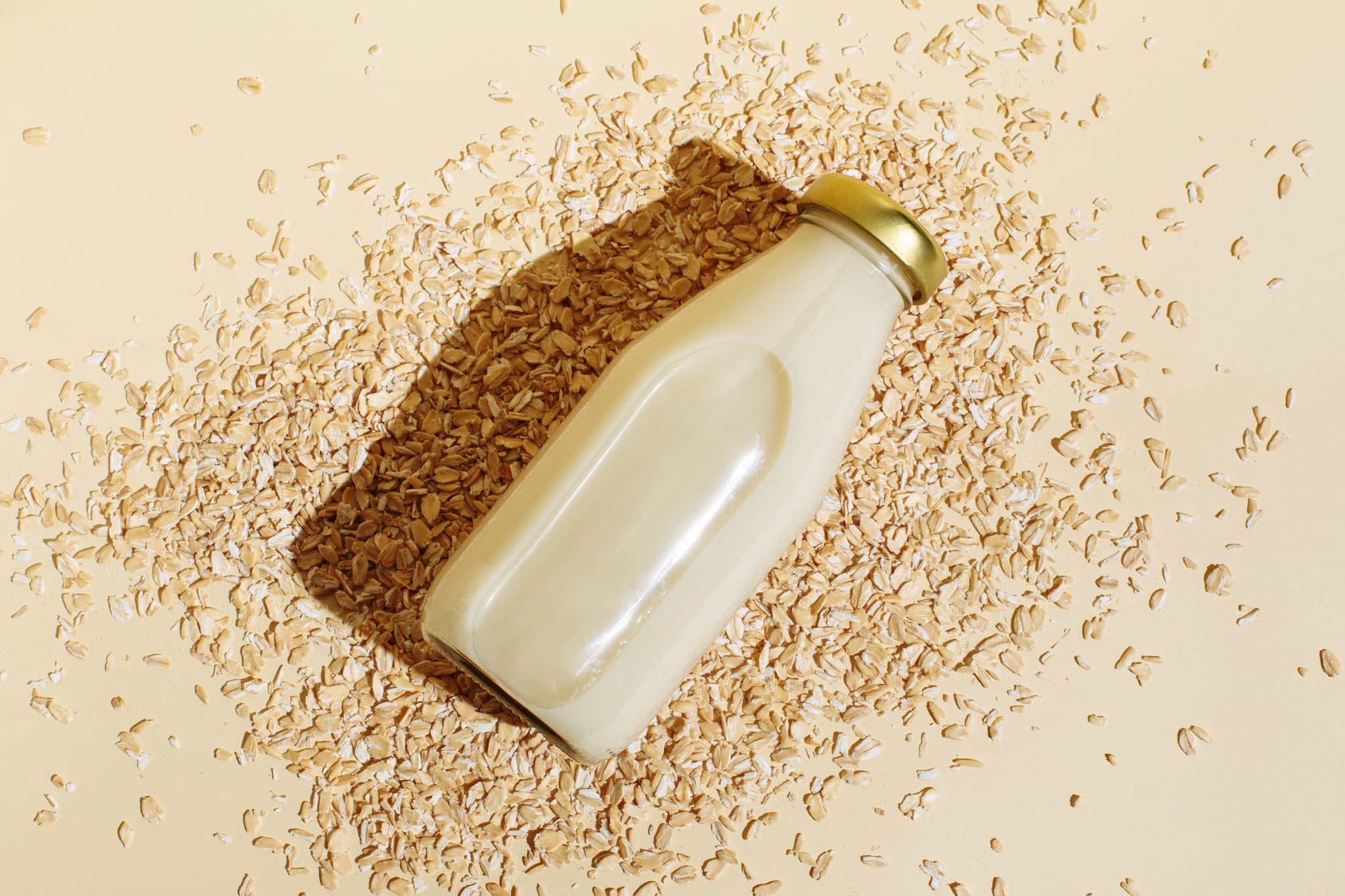 Oat milk in glass bottle and oatmeal flakes on beige background; is oat milk good for you?