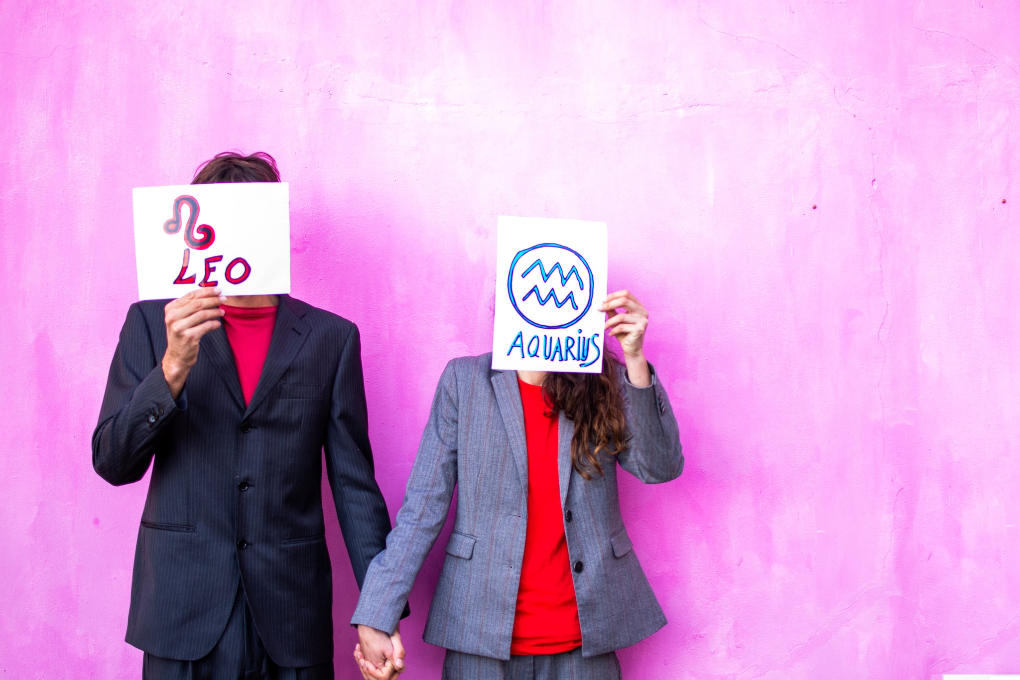 a young couple holding a sign with their zodiac sign. Hidden face, unrecognizable person. Pink background.