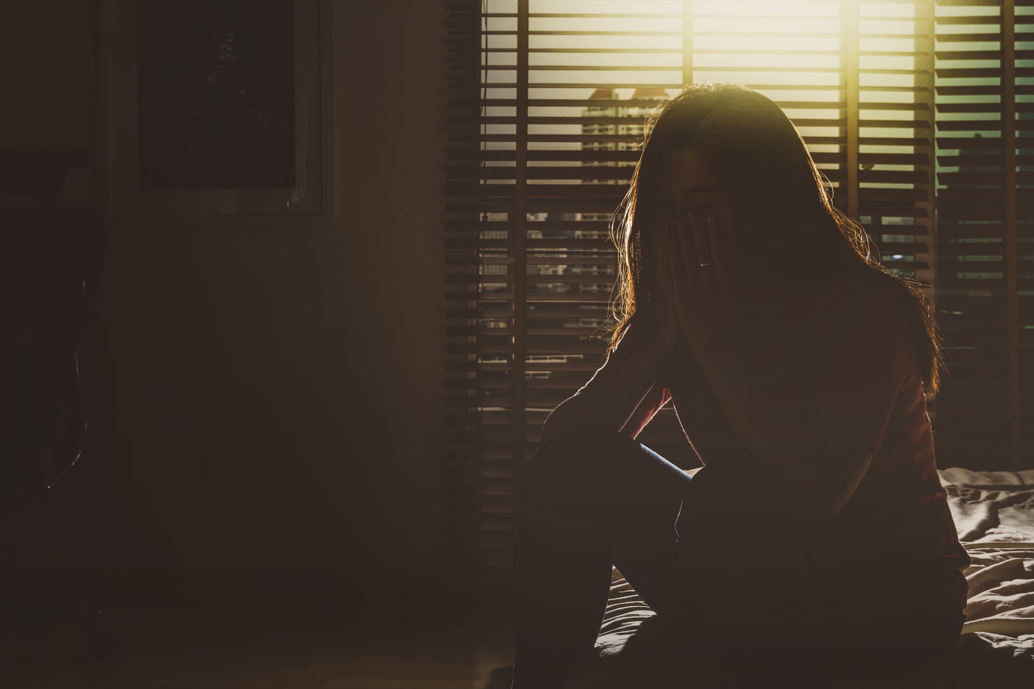 depressed Women sitting head in hands on the bed in the dark bedroom with low light environment, dramatic concept