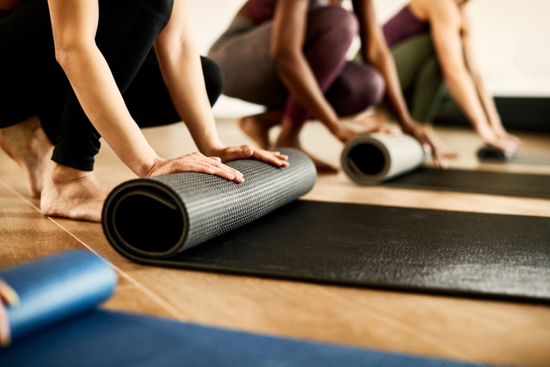 Close-up of athletic women preparing their exercise mats for sports training at health club. Focus is on woman in black.