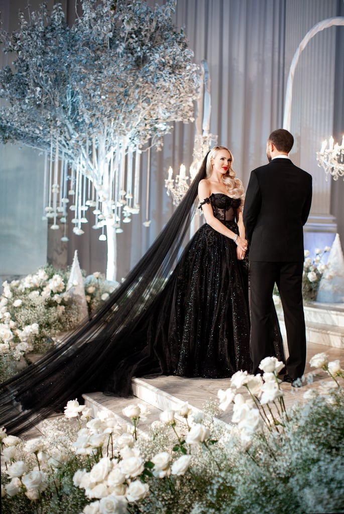 Dramatic? Check. Over the top? Check. Statement making in every way possible? Check check. There are few people who can pull off a black wedding dress, and Christine Quinn from Selling Sunset absolutely checks off the boxes. It should come as no surprise that the chic real estate agent from Netflix's hit reality series pulled out all the stops for her gothic, winter-wonderland-themed wedding, but when her and Christian's nuptials aired during the season three finale of the show, viewers were blown away by the detail and dedication to the theme. The energy was immediately palpable when she stepped out of a carriage in her bespoke black gown designed by Galia Lahav — her first dress of the evening, that is.
"Christine knew that she desired something unique and dramatic."
POPSUGAR chatted with Galia about working with Christine to design her gorgeous wedding dresses, both for the ceremony and the reception, and to say that Christine's vision was beautifully brought to life would be an understatement. "Christine knew that she desired something unique and dramatic; she was very enthusiastic about a custom dress that would be totally unique," Galia shared, adding that with Christine's guests in white and not a soft tone in sight, she was bound to stand out. 
Viewers got to see Christine's first dress appointment during the show and immediately knew it would be one of a kind. Galia was able to add all the special elements usually found on a typical bridal look, including the "sparkle, embellishments, and lace" to complete the bride's look. The ballgown featured a sheer black bustier top with off-the-shoulder straps, shimmering details, and black roses embroidered from the top all the way down through the tulle bottom. Every element of the dress sparkled with detail.

    Related:

            
            
                                    
                            

            The "Selling Sunset" Cast on Their Personal Style and Favorite Outfits From Season 5
        
    
"Christine described herself as a 'Gothic Barbie,' and our stylist made sure the custom appliqué on the ballgown reflected that style," Galia said. "We knew that a gothic English rose look would be a perfect fit for that lace . . . Christine decided she wanted to add one last pop of drama to her looks, so we decided on an incredible seven-meter-long black veil to make her walk down the aisle feel even more regal!" That's right, "incredible" is the perfect word to describe the spectacular veil that was over 22 feet long.
For Christine's reception dress, she upped the sexiness factor and put her own spin on the designer's Thelma gown. The supertight dress has a flattering mermaid shape with mesh cutouts down the legs, and with Christine's vision and Galia's magic touch, it was customized to perfectly capture the bride's ornate style. "We altered the original design to match Christine's vision of a sexy nighttime glam look but still with that elegant, bridal touch," Galia said. "We customized the original design by adding feathers to the skirt, dramatic points to the cups, and black Swarovski crystals to the bodice to ensure Christine's look was absolutely one of a kind." Both gowns were entirely made by hand in just two months!
Ahead, see some of the stunning photos of Christine's bespoke Galia Lahav wedding dresses, which the designer confirms she was "involved in every part of the process" of designing.

    Related:

            
            
                                    
                            

            Future Brides, Shop the 54 Most Stunning Wedding Dresses For 2021