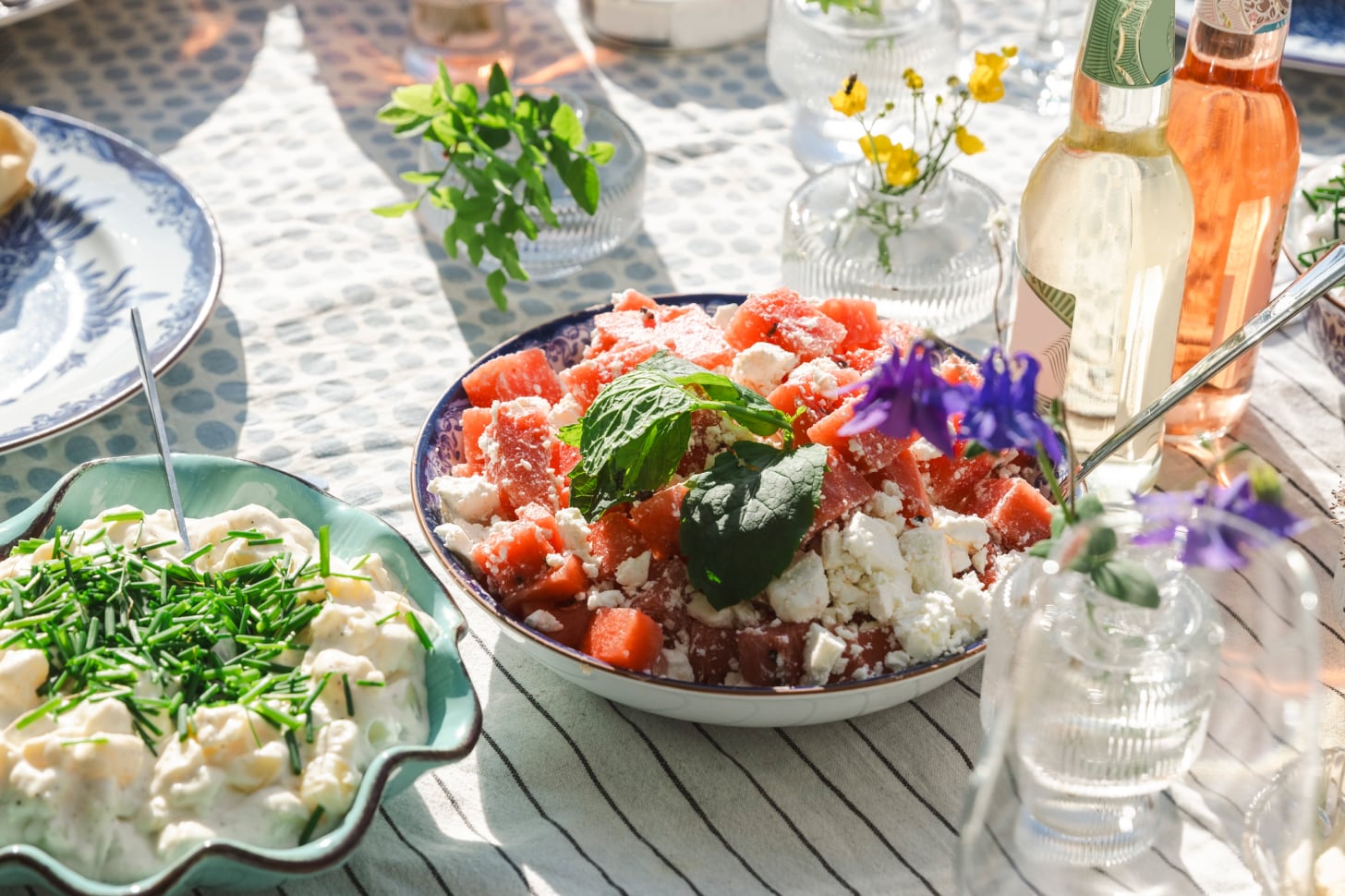 A table full of dishes with watermelon salad and potato salad for a dinner party in hostingcore style.