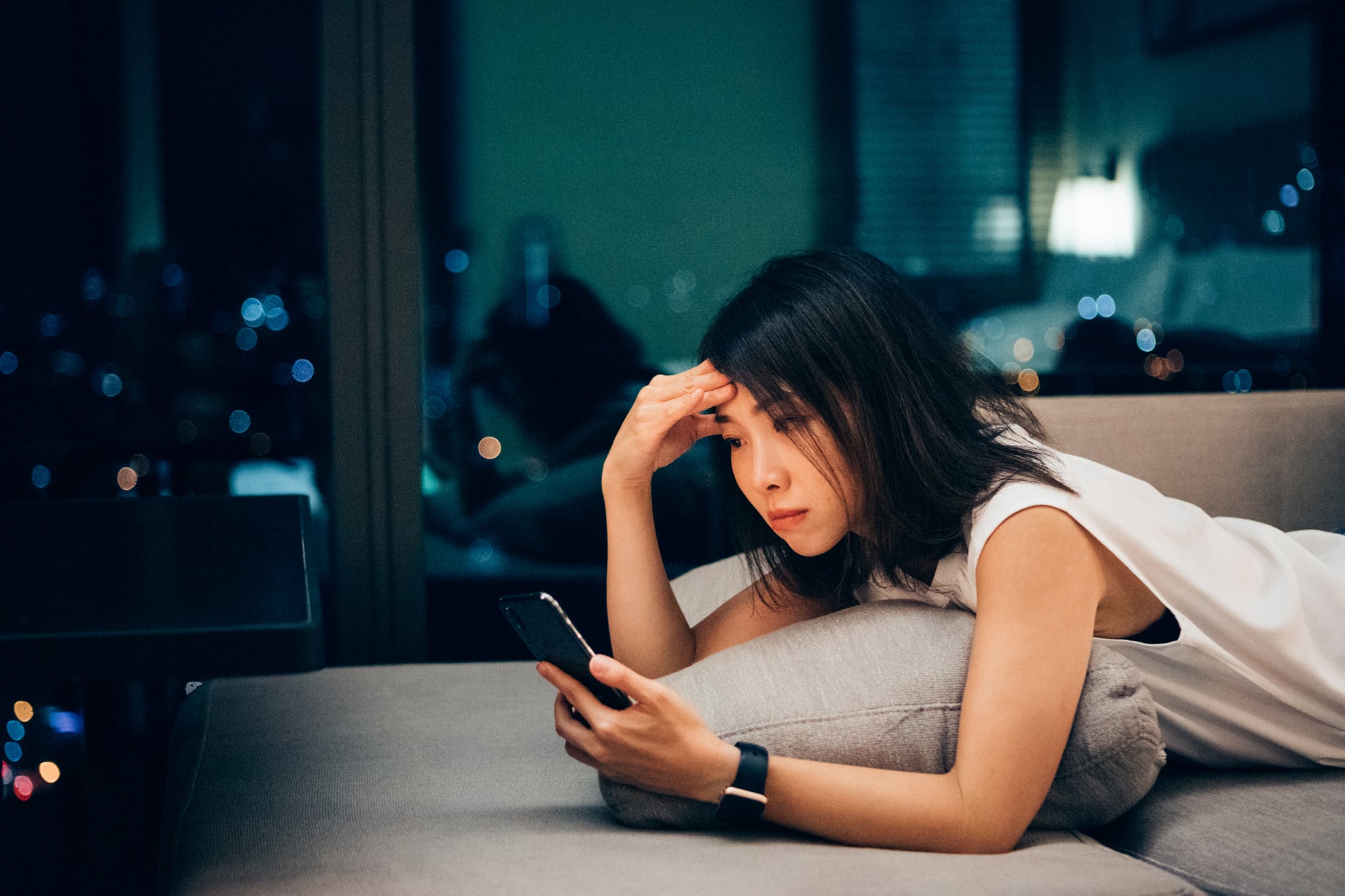 Young Asian businesswoman working late and checking work email on mobile at home