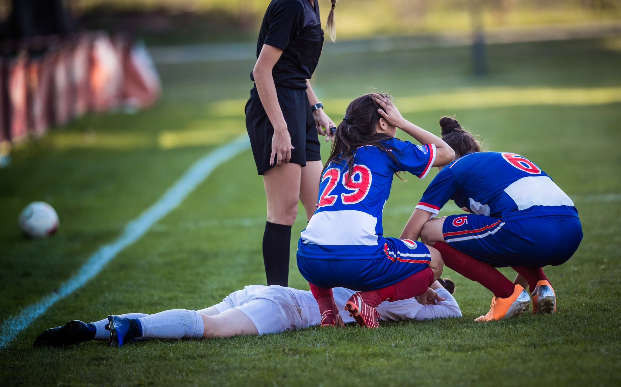 Group of female soccer players and referee gathering around injured player on playing field.