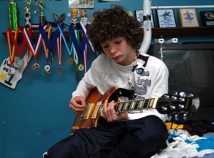 "He's proud that he learned how to play guitar completely on his own. He refuses to take any lessons, other than watching YouTube. Here he is, playing one of his guitars, with some of his running medals behind him."