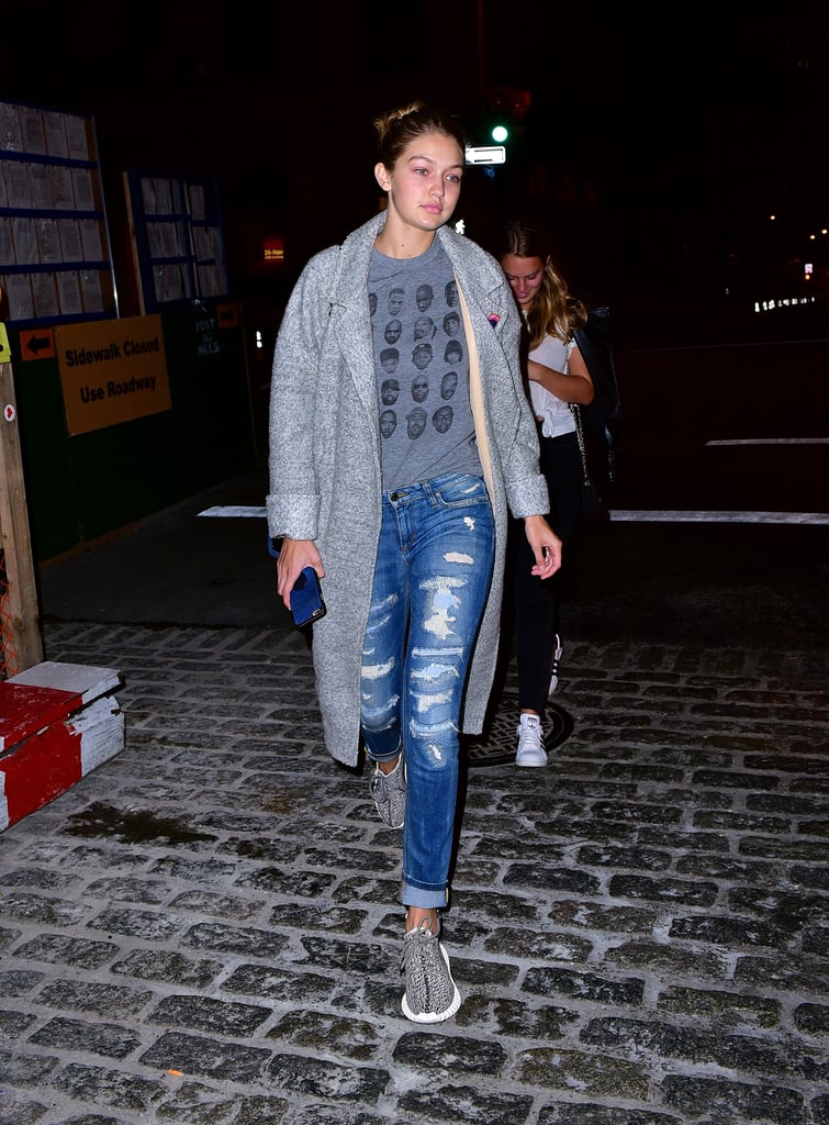 Wearing distressed denim with a graphic tee, gray jacket, and Yeezy sneakers.